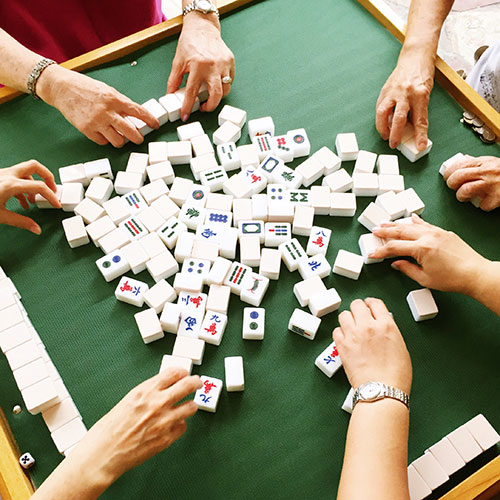 一個打麻將的環境，有三名玩家在抓牌、綠色牌尺、綠色麻將子以及堆疊好的麻將牌。